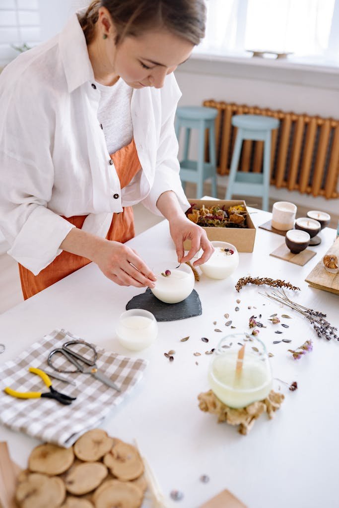Woman crafting candles with dried flowers in a workshop setting.